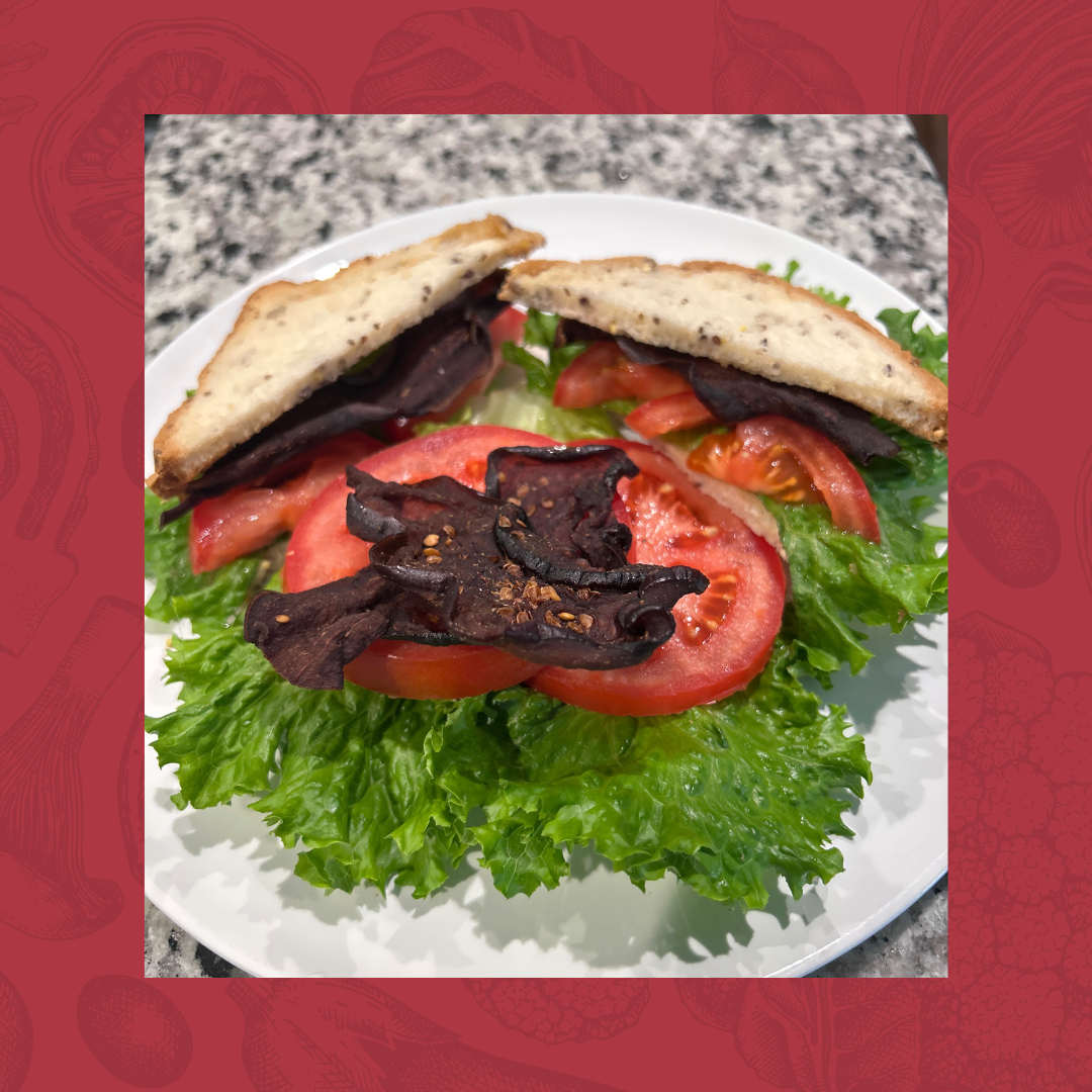 BLT sandwich with lettuce, tomatoes, and vegan jerky on a white plate.